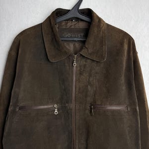 May include: A brown suede jacket with a zipper closure and two zippered pockets. The jacket has a label that reads "GO WEST".