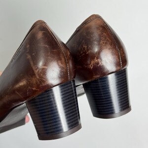 Puede incluir: Un par de zapatos de tac&oacute;n de cuero marr&oacute;n. Los zapatos tienen un tac&oacute;n de bloque y una punta redondeada. El cuero tiene un aspecto desgastado. Los tacones miden aproximadamente 5 cm de alto.