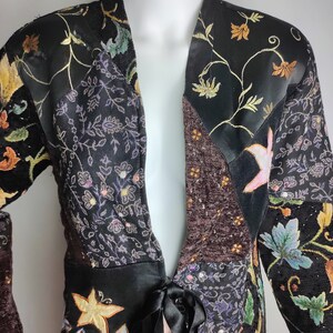 May include: A black and brown patchwork jacket with floral embroidery and a tie at the waist.