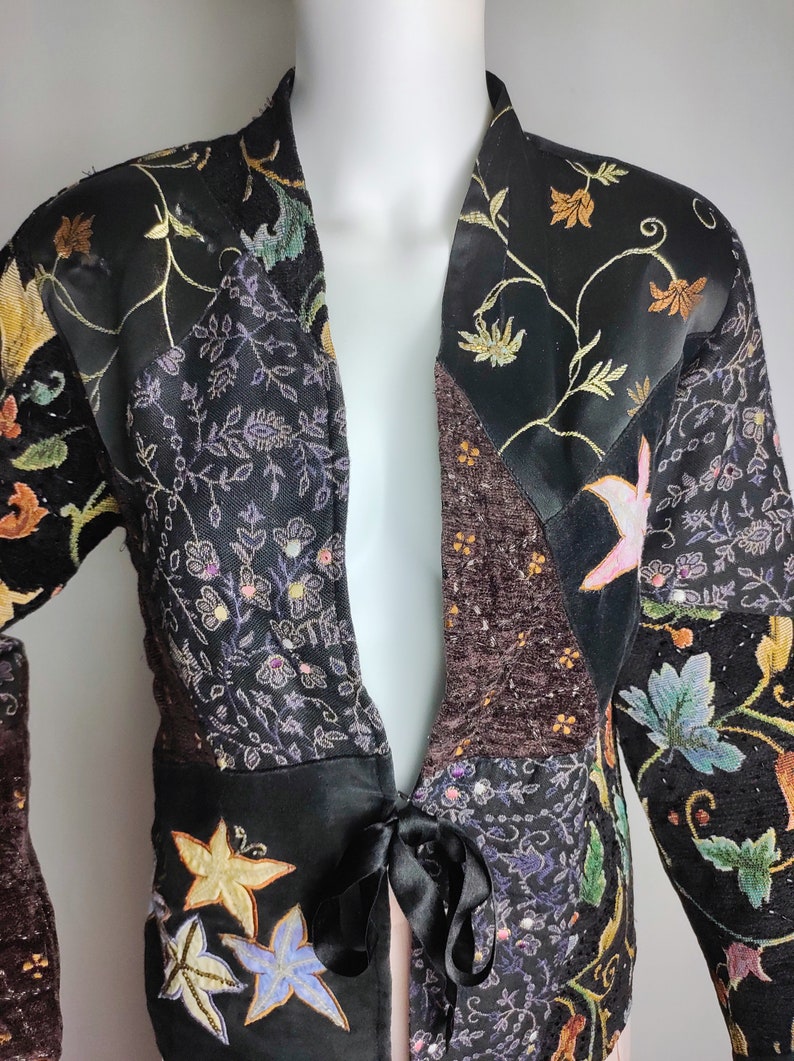 May include: A black and brown patchwork jacket with floral embroidery and a tie at the waist.