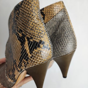 May include: A pair of brown and black snakeskin heeled ankle boots with a pointed toe.