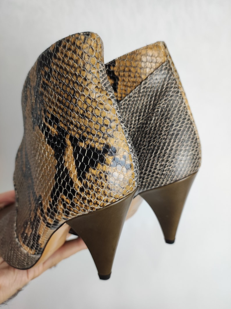 May include: A pair of brown and black snakeskin heeled ankle boots with a pointed toe.