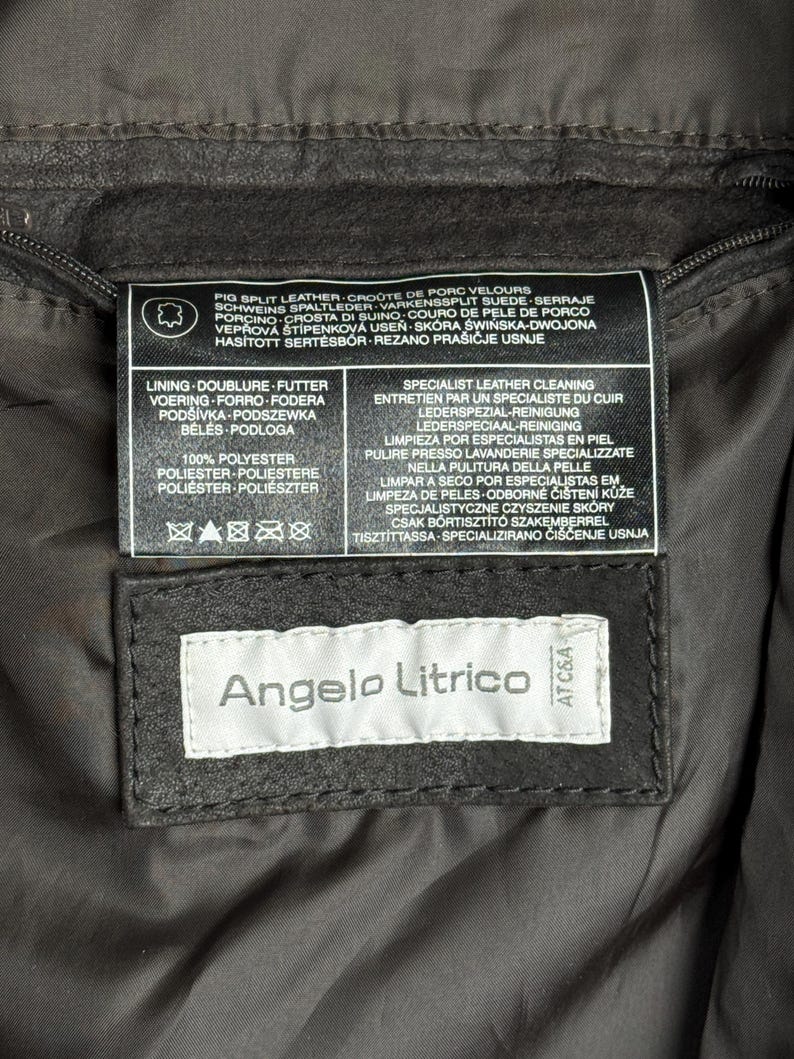 Puede incluir: Primer plano de una etiqueta de chaqueta de cuero marr&oacute;n oscuro. La etiqueta dice "Angelo Litrico" en texto blanco sobre un fondo negro. Texto adicional en la etiqueta detalla los materiales e instrucciones de cuidado de la chaqueta.