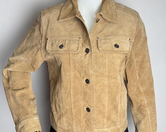 Könnte beinhalten: Hellbraune Wildlederjacke mit Kragen, zwei Brusttaschen und Knopfverschlüssen. Die Jacke hat lange Ärmel und eine taillierte Passform. Das Kleidungsstück wird auf einer Schaufensterpuppe präsentiert.