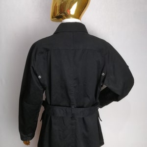 May include: Black belted jacket with long sleeves and a collar. The jacket has two pockets on the front and two on the sides.