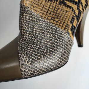 May include: Close-up of a brown, black, and green snakeskin heeled boot with a pointed toe.