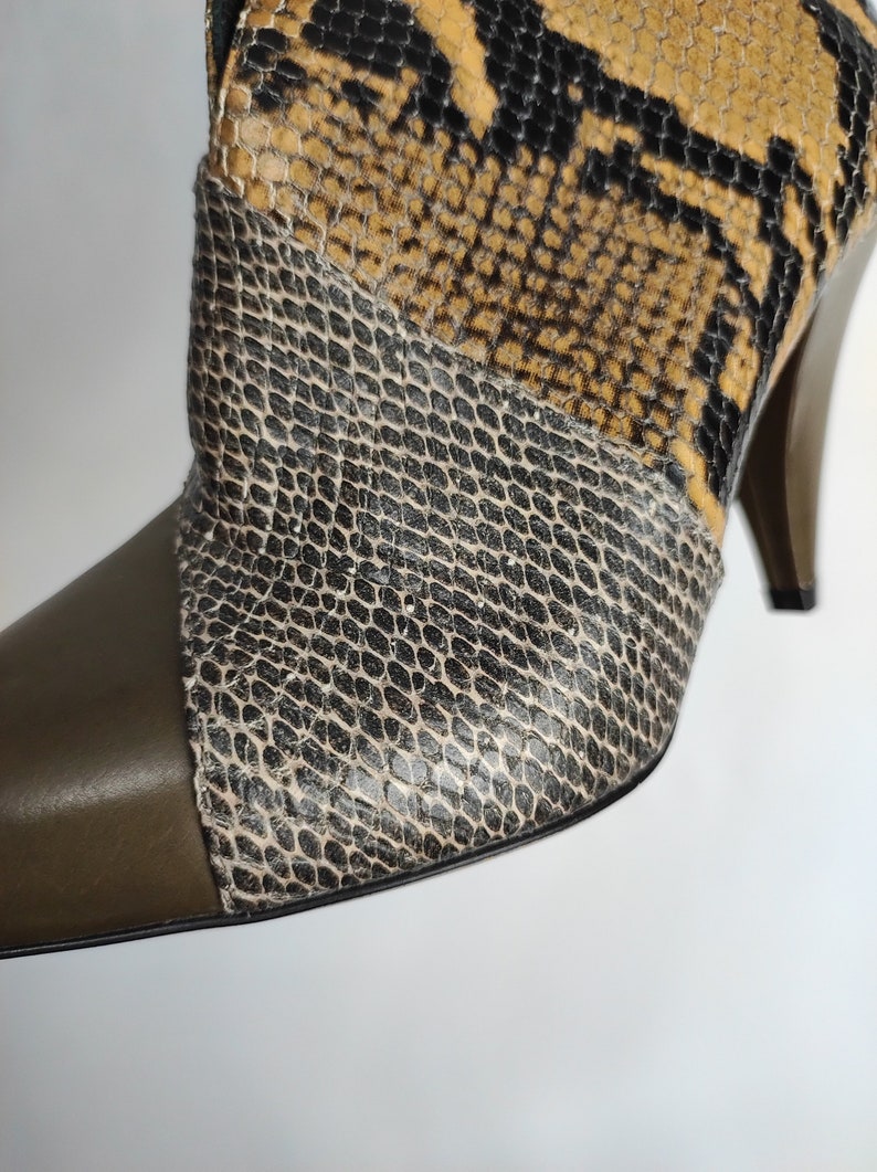 May include: Close-up of a brown, black, and green snakeskin heeled boot with a pointed toe.