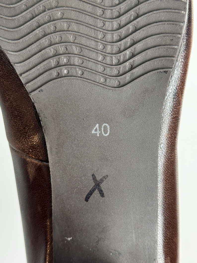Puede incluir: Primer plano de la suela de un zapato de cuero marr&oacute;n. La suela es de color gris oscuro con un patr&oacute;n ondulado y texturizado y el n&uacute;mero "40" impreso en blanco. Una "X" negra est&aacute; marcada en la suela.
