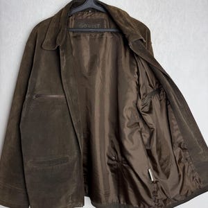 May include: A brown suede jacket with a zipper closure and a Go West label on the inside. The jacket has a stand-up collar and two pockets on the front.