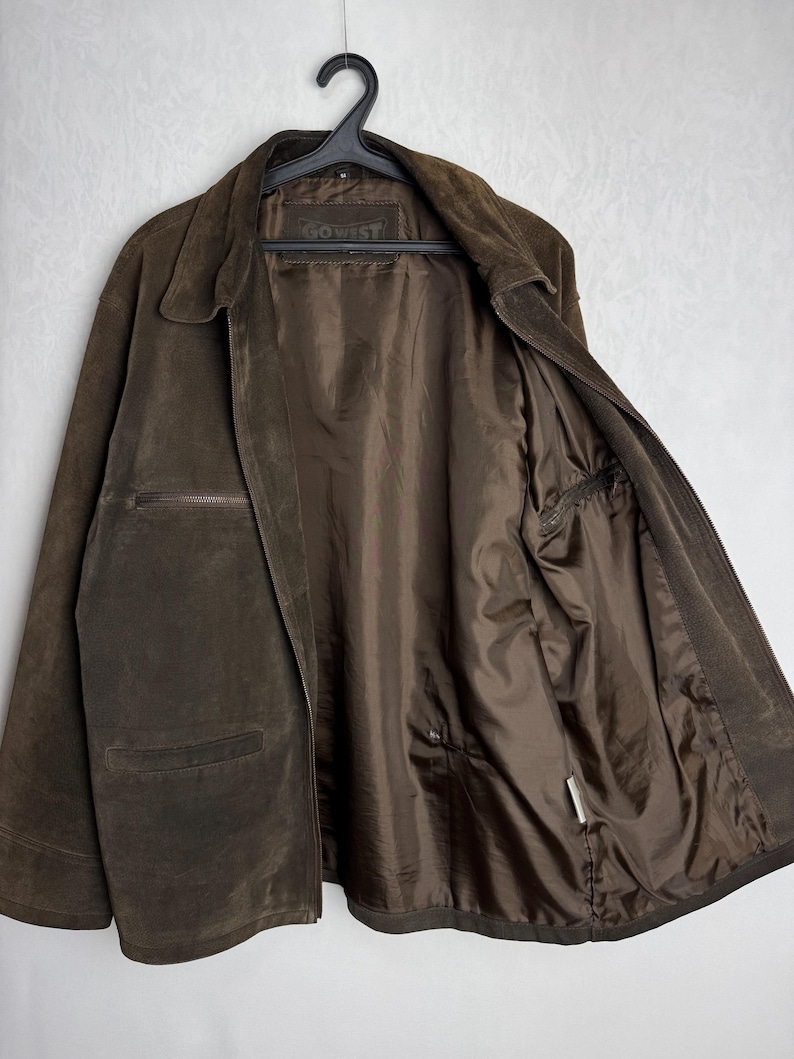 May include: A brown suede jacket with a zipper closure and a Go West label on the inside. The jacket has a stand-up collar and two pockets on the front.
