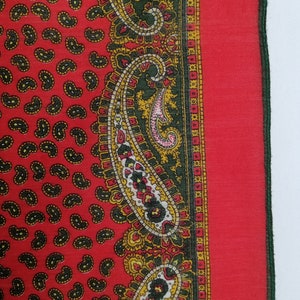 Puede incluir: Textil rojo con estampado de cachemir y borde detallado. El textil presenta un patr&oacute;n repetitivo de formas de cachemir negras sobre un fondo rojo. El borde incluye dise&ntilde;os de cachemir verdes, amarillos y rojos.