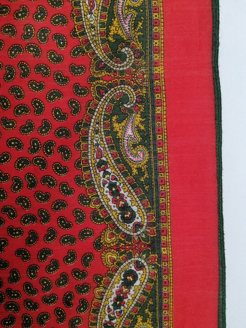 Puede incluir: Textil rojo con estampado de cachemir y borde detallado. El textil presenta un patr&oacute;n repetitivo de formas de cachemir negras sobre un fondo rojo. El borde incluye dise&ntilde;os de cachemir verdes, amarillos y rojos.