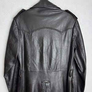 May include: Black leather coat hanging on a black hanger. The coat has a classic design with a notched collar, shoulder epaulets, and a button closure. The coat is made of a smooth, shiny leather material.