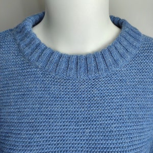 May include: A light blue knitted jumper with a round neckline.