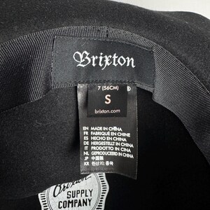 Puede incluir: Sombrero fedora de fieltro negro con una cinta negra y una etiqueta de Brixton Supply Company. El sombrero es talla 7 (56 cm) y talla S.
