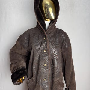 Peut inclure: Un manteau en daim marron avec une capuche et des poignets doublés de fausse fourrure. Le manteau a un motif zèbre et une fermeture à boutons.