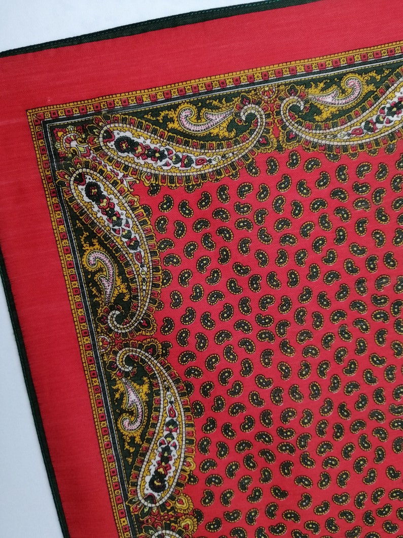 Puede incluir: Un pa&ntilde;uelo rojo con estampado de cachemira y borde verde oscuro. El pa&ntilde;uelo presenta un patr&oacute;n repetido de peque&ntilde;as formas de cachemira negras sobre un fondo rojo. El borde tiene un dise&ntilde;o detallado con elementos de cachemira amarillos, negros y blancos.