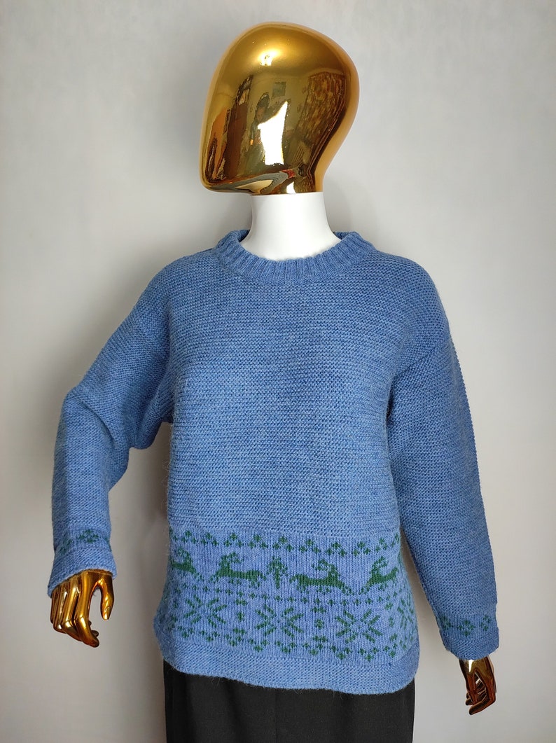 May include: A blue knitted jumper with a green reindeer pattern around the bottom hem.
