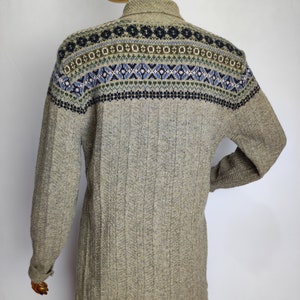 May include: A light brown sweater with a patterned yoke featuring blue, green, and white geometric designs. The long-sleeved sweater has a ribbed texture and a collared neckline. The back view of the sweater is shown on a mannequin.