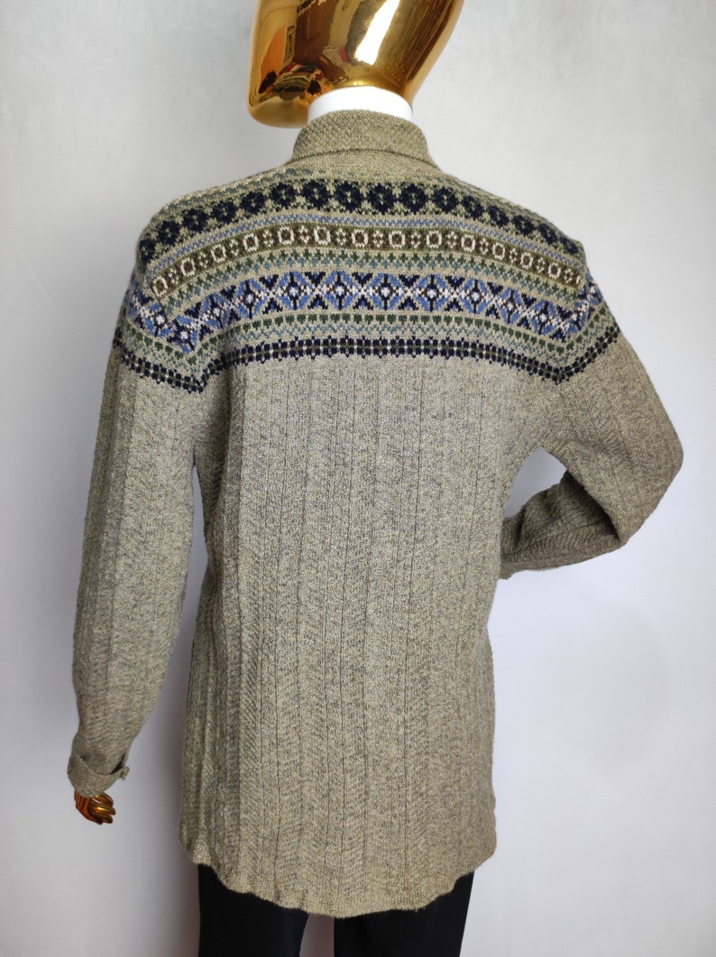 May include: A light brown sweater with a patterned yoke featuring blue, green, and white geometric designs. The long-sleeved sweater has a ribbed texture and a collared neckline. The back view of the sweater is shown on a mannequin.