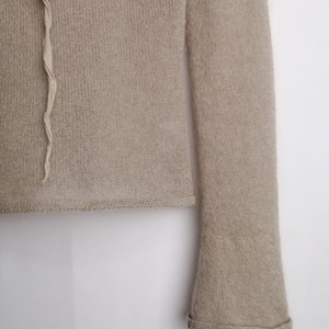 Puede incluir: Un su&eacute;ter de punto beige con mangas largas y un ribete con volantes en la parte inferior de las mangas.