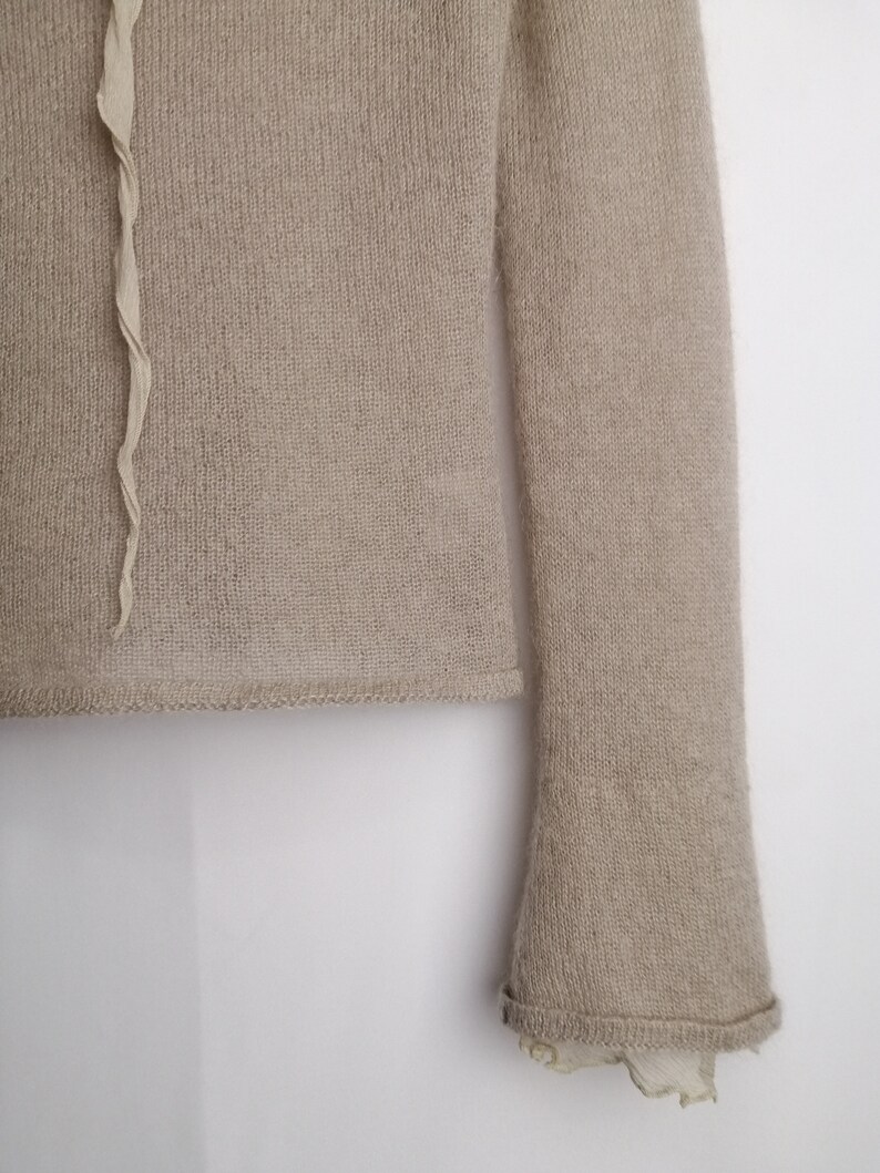 Puede incluir: Un su&eacute;ter de punto beige con mangas largas y un ribete con volantes en la parte inferior de las mangas.