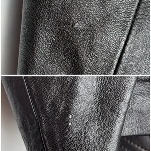 May include: Close-up of black leather jacket material. The leather has a textured surface with small imperfections. The image shows the jacket's seams and the edge of the sleeve, highlighting the details of the garment's construction.