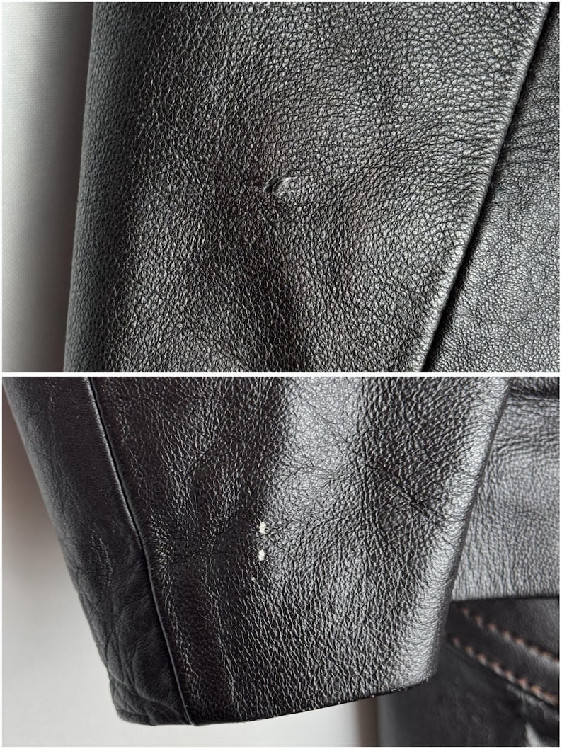 May include: Close-up of black leather jacket material. The leather has a textured surface with small imperfections. The image shows the jacket's seams and the edge of the sleeve, highlighting the details of the garment's construction.