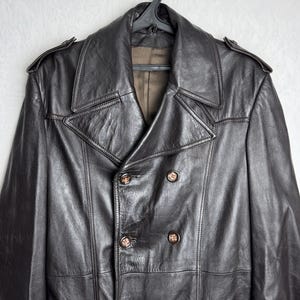 May include: A dark brown leather coat with a double-breasted design, featuring large lapels and decorative buttons. The coat is hanging on a black hanger, showcasing its classic style and texture.