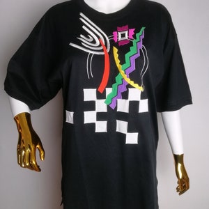 May include: Black t-shirt with a colourful abstract design featuring geometric shapes, lines, and a chequered pattern.