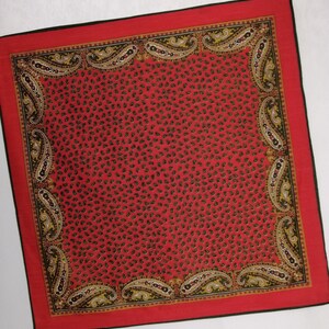 Puede incluir: Un pa&ntilde;uelo cuadrado rojo con borde negro y estampado de cachemira. El centro del pa&ntilde;uelo est&aacute; cubierto de peque&ntilde;as formas de cachemira negras. El borde presenta dise&ntilde;os de cachemira m&aacute;s grandes en negro, amarillo y blanco.