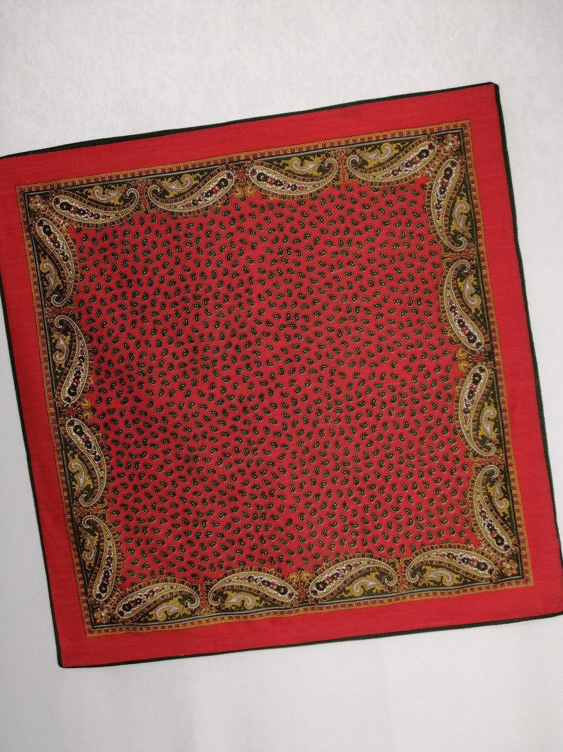 Puede incluir: Un pa&ntilde;uelo cuadrado rojo con borde negro y estampado de cachemira. El centro del pa&ntilde;uelo est&aacute; cubierto de peque&ntilde;as formas de cachemira negras. El borde presenta dise&ntilde;os de cachemira m&aacute;s grandes en negro, amarillo y blanco.