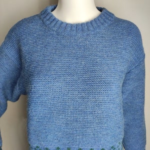 May include: A blue knitted jumper with a green and blue patterned design at the bottom.