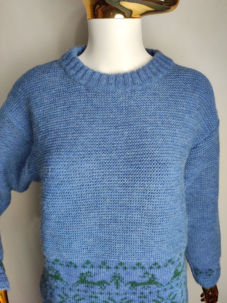 May include: A blue knitted jumper with a green and blue patterned design at the bottom.