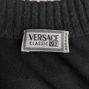 以下が含まれることがあります： 黒いニット生地に、「VERSACE CLASSIC V2 MADE IN ITALY」と書かれた白いラベルが付いている。