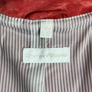 Puede incluir: Primer plano del interior de una chaqueta de ante roja. El forro es blanco con finas rayas verticales marrones. Una etiqueta blanca con el texto "Charles V&ouml;gele" est&aacute; cosida en el forro. Una etiqueta m&aacute;s peque&ntilde;a muestra la talla "42".