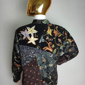 May include: A black quilted jacket with a patchwork design featuring floral embroidery and sequins. The jacket has a mandarin collar and long sleeves.