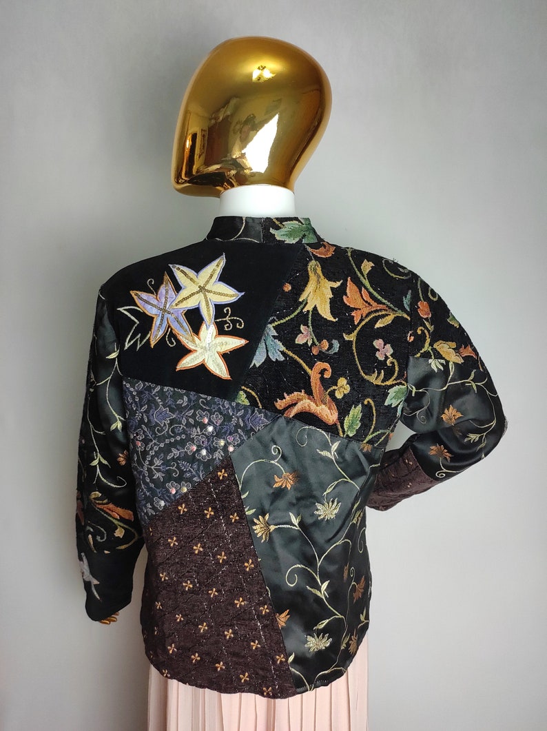 May include: A black quilted jacket with a patchwork design featuring floral embroidery and sequins. The jacket has a mandarin collar and long sleeves.
