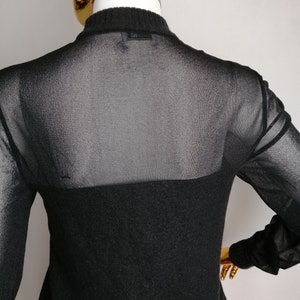 以下が含まれることがあります： 黒いシアーロングスリーブセーター。黒いニットのボトムレイヤーが付いています。セーターの背面には、「Equipment」と書かれた小さな黒いラベルが付いています。