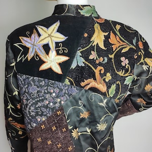 May include: A black quilted jacket with a patchwork design featuring different floral patterns and embroidered details. The jacket has a high collar and long sleeves.