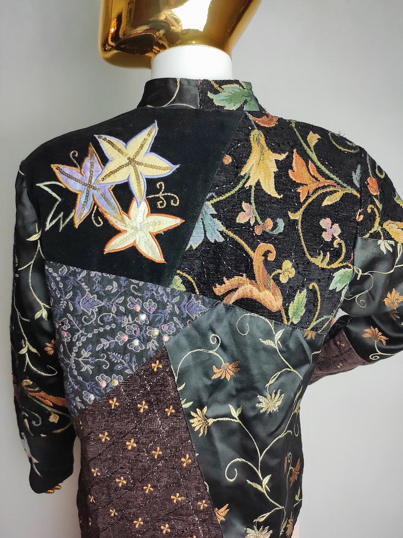 May include: A black quilted jacket with a patchwork design featuring different floral patterns and embroidered details. The jacket has a high collar and long sleeves.