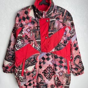 May include: A red, black, and white patterned ski jacket with a zipper closure and a button at the neck.