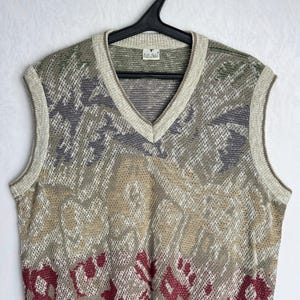May include: A vintage V-neck sweater vest with a patterned design in shades of green, gray, beige, and burgundy. The vest is sleeveless and has a ribbed trim around the neckline and armholes. The garment is hanging on a black hanger.