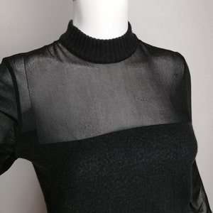 以下が含まれることがあります： 黒のロングスリーブシャツ。上部に透き通ったメッシュパネル、下部に無地のニット素材を使用しています。