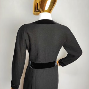 K&ouml;nnte beinhalten: Schwarzes Kleid mit Samtkragen und G&uuml;rtel. Das Kleid hat einen strukturierten Stoff und lange &Auml;rmel.