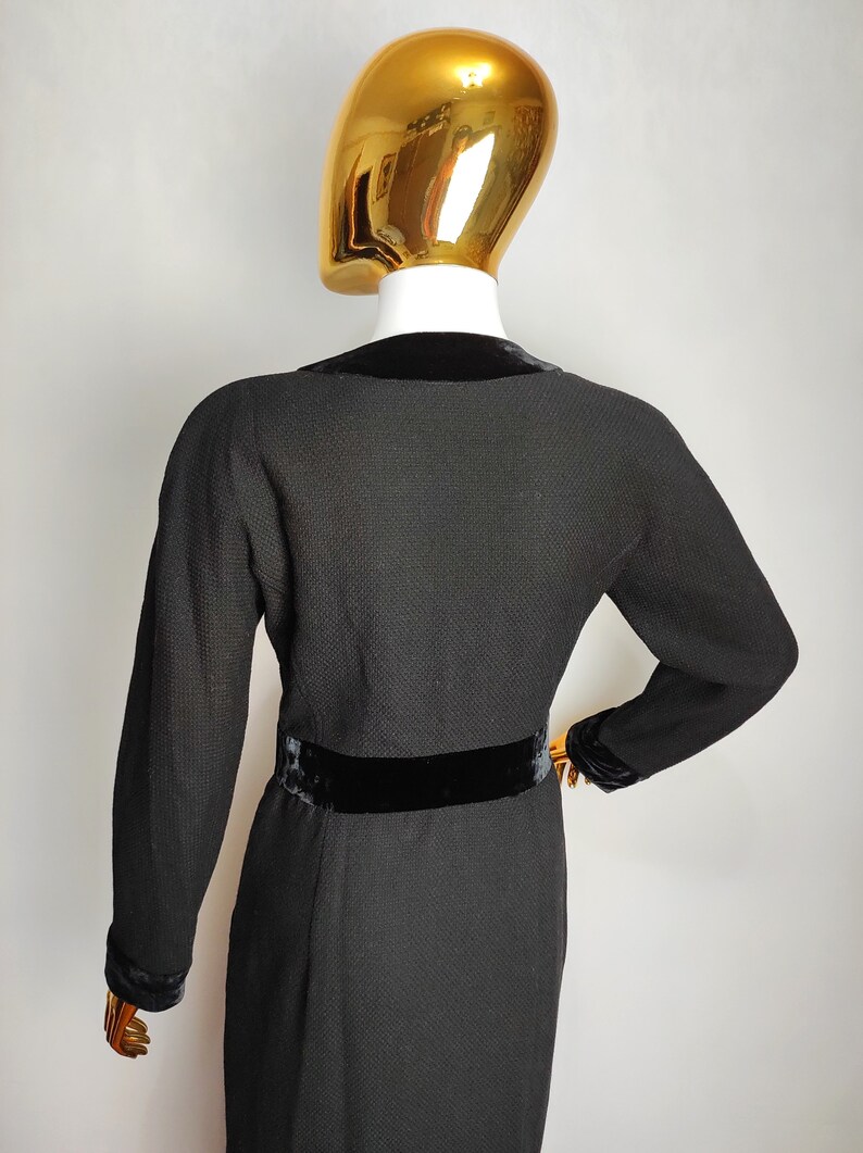 K&ouml;nnte beinhalten: Schwarzes Kleid mit Samtkragen und G&uuml;rtel. Das Kleid hat einen strukturierten Stoff und lange &Auml;rmel.