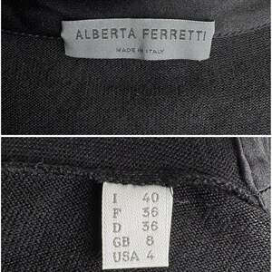 K&ouml;nnte beinhalten: Ein schwarzer Strickcardigan mit einem wei&szlig;en Etikett, auf dem "Alberta Ferretti" und "Made in Italy" steht. Das Etikett zeigt auch die Gr&ouml;&szlig;e in verschiedenen Gr&ouml;&szlig;ensystemen: I 40, F 36, D 36, GB 8, USA 4.