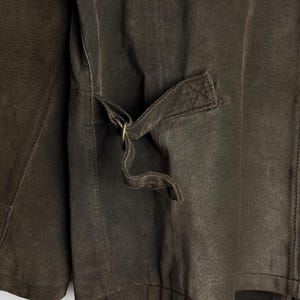 May include: A brown leather jacket with a zipper closure and a strap with a metal buckle on the back.
