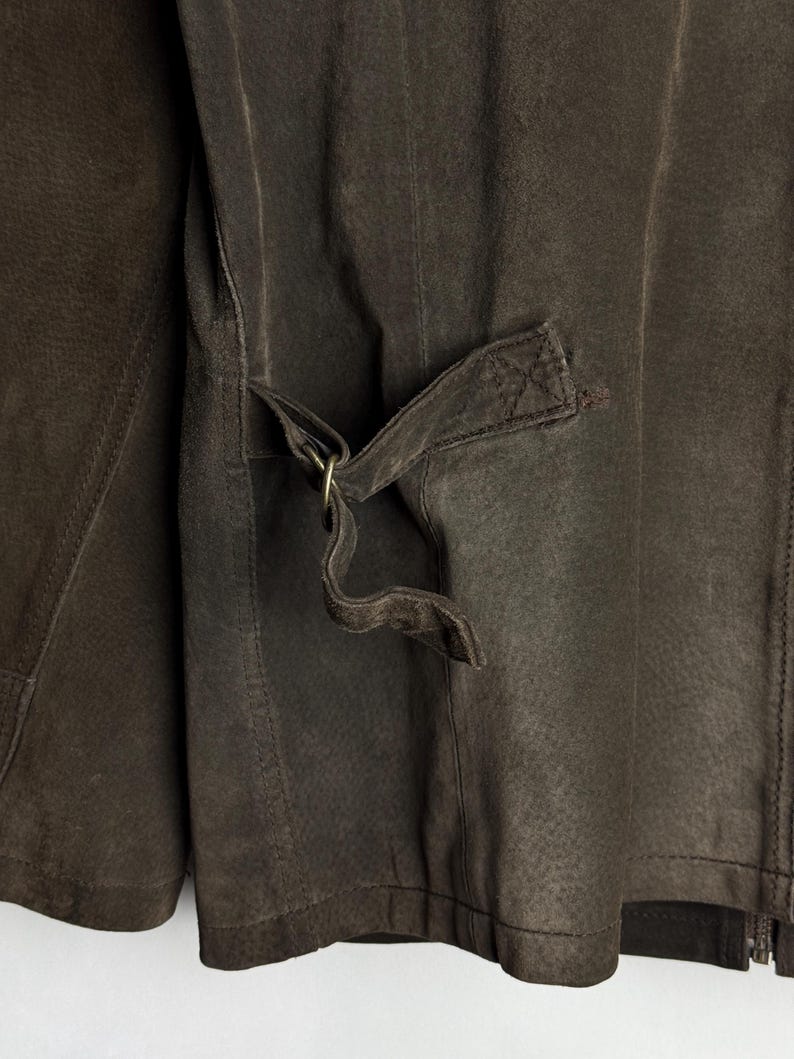 May include: A brown leather jacket with a zipper closure and a strap with a metal buckle on the back.