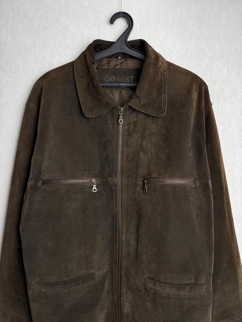 May include: A brown suede jacket with a zipper closure and multiple pockets. The jacket has a label that reads "GO WEST".